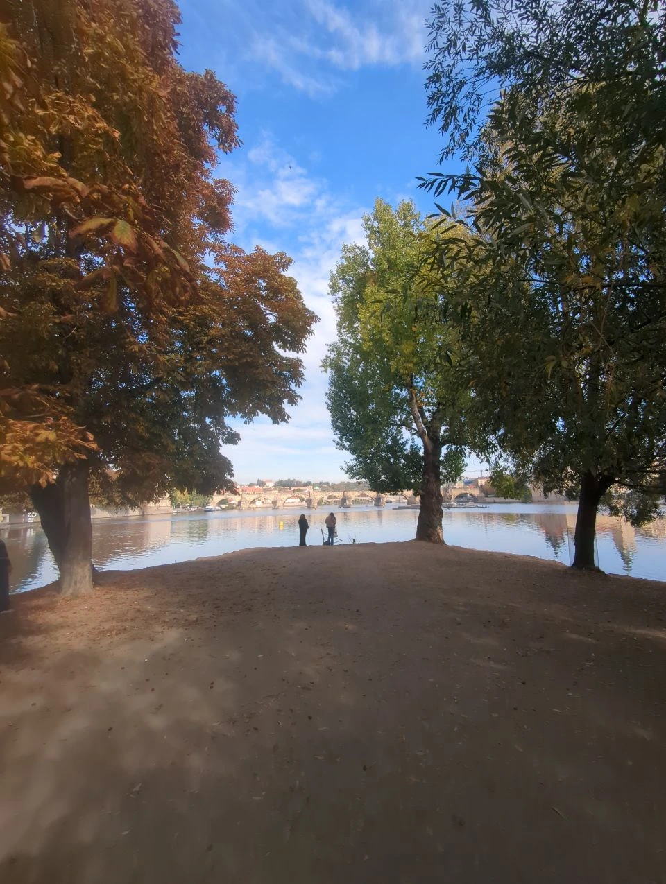 Autumn trees frame a view across the Vltava from Shooter’s Island, with Charles Bridge visible beyond the river.