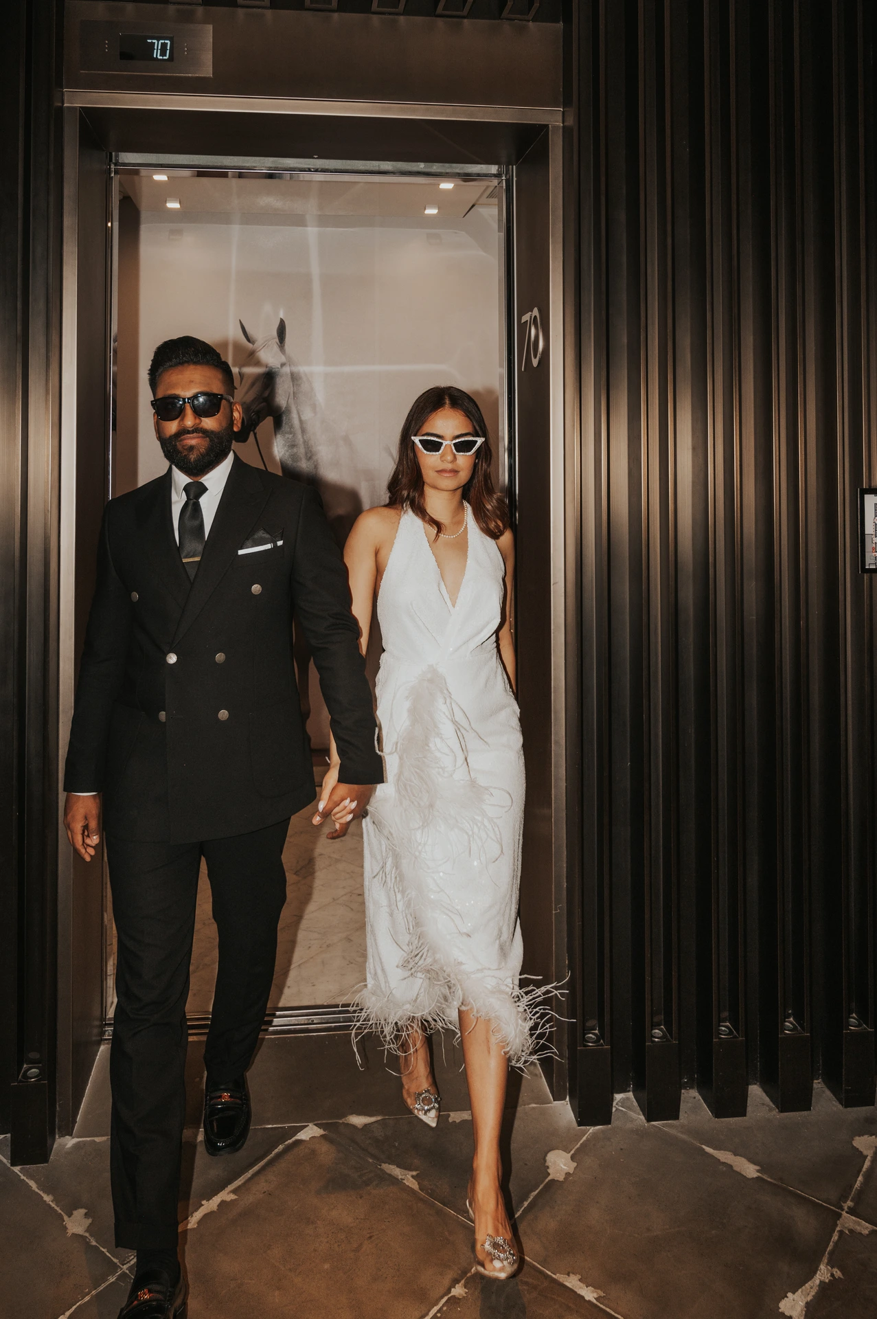 A stylish couple walks out of an indoor doorway in formal outfits during an editorial-style Dubai photoshoot.