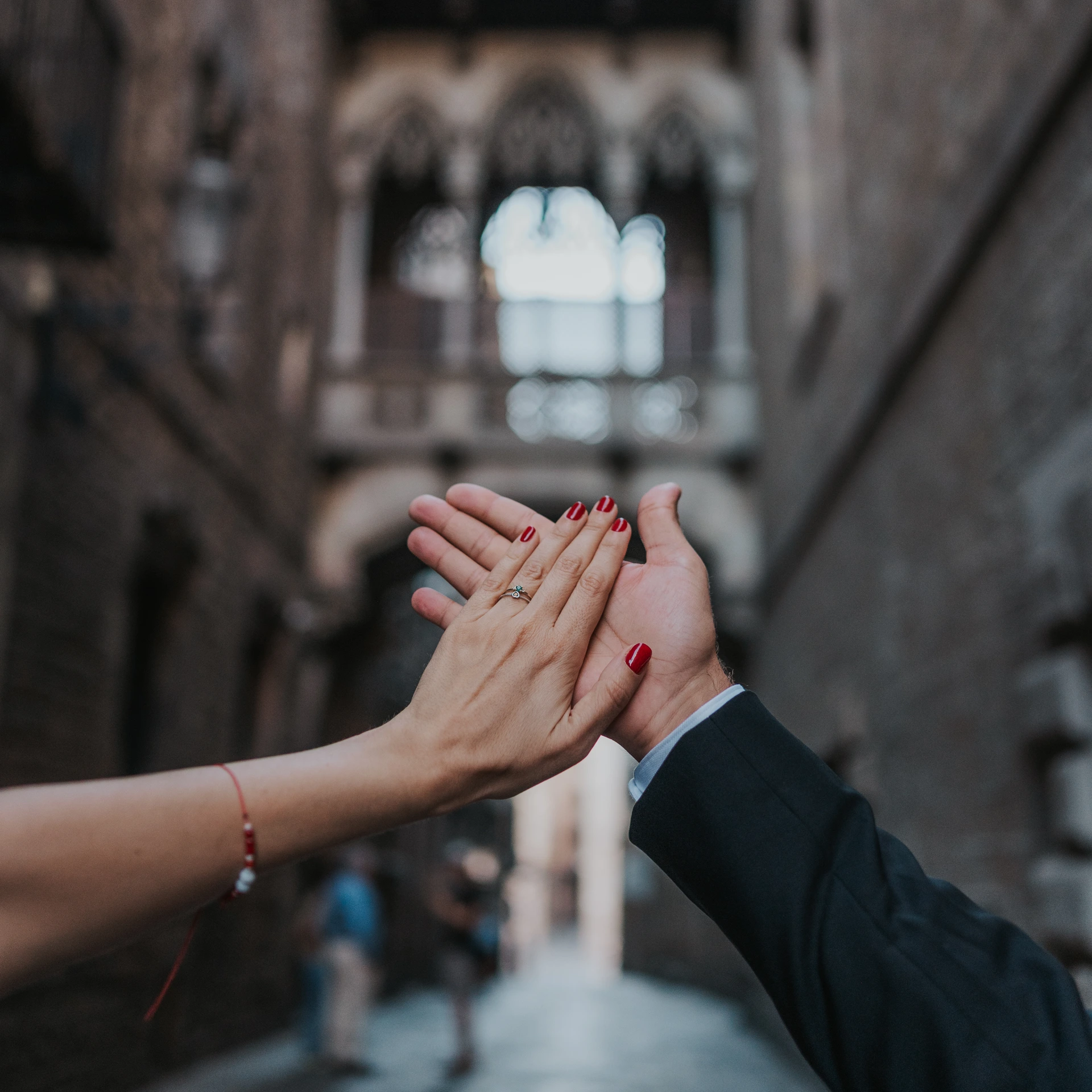 Two hands frame an engagement ring beneath a softly blurred stone arcade in Barcelona's Gothic Quarter.
