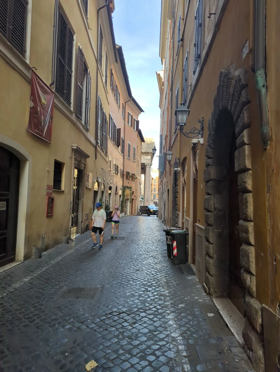 Rome Photoshoot Shoes - Cobblestone Walk Two visitors in trainers and casual summer clothes walk along a narrow cobbled street in central Rome.