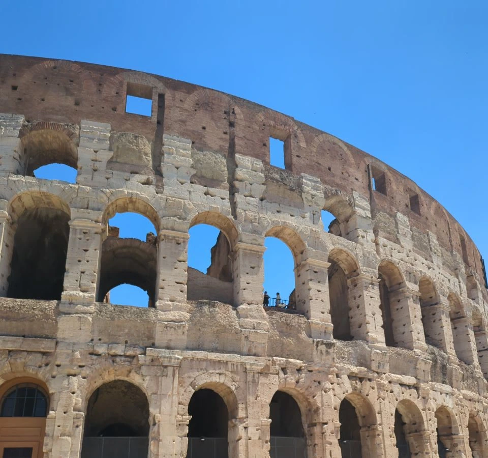 The Colosseum’s curved facade fills the frame with repeating stone arches against blue sky, illustrating a close Rome photoshoot angle.