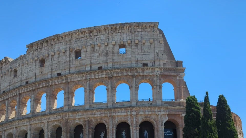 The Colosseum’s curving stone arcades rise beneath a clear blue sky, creating a bold landmark backdrop for a Rome photoshoot.