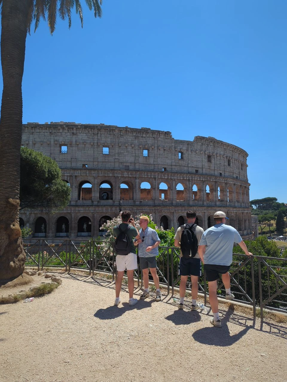 Rome Group Photoshoot Outfits - Colosseum View Four visitors wearing blue, green and neutral casual outfits stand at a viewpoint overlooking the Colosseum in Rome.