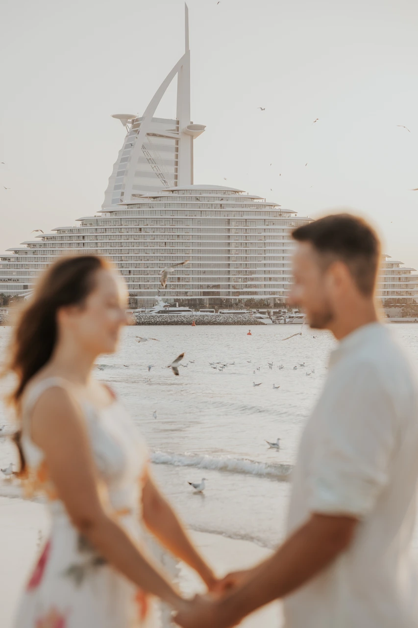 Couple photoshoot dubai costs - Soft-focus beach portrait A soft-focus couple portrait on the beach in Dubai with Burj Al Arab and a resort backdrop behind them.