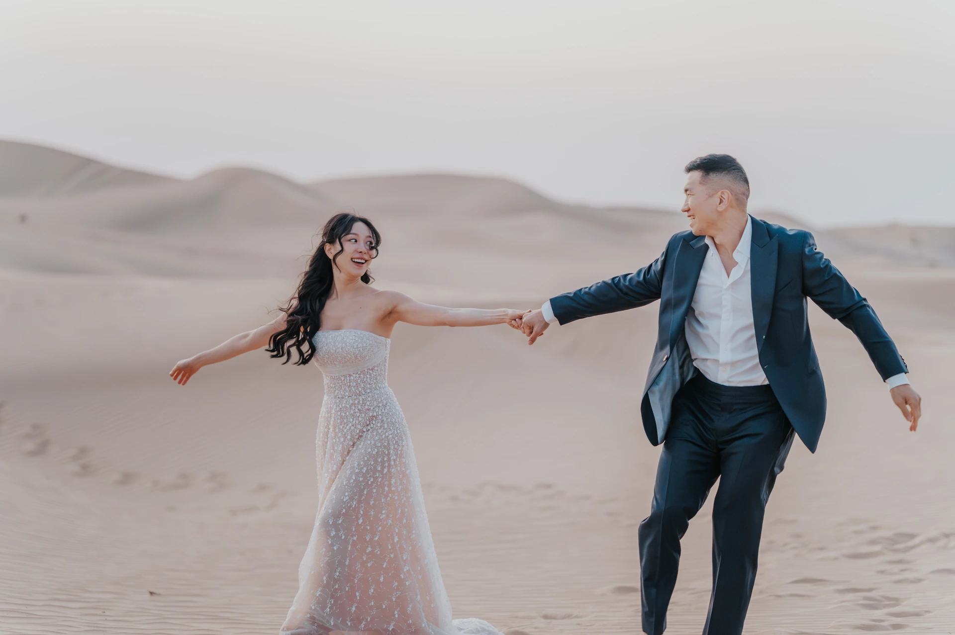 A couple holds hands while walking on Dubai desert dunes during a romantic sunset photoshoot.