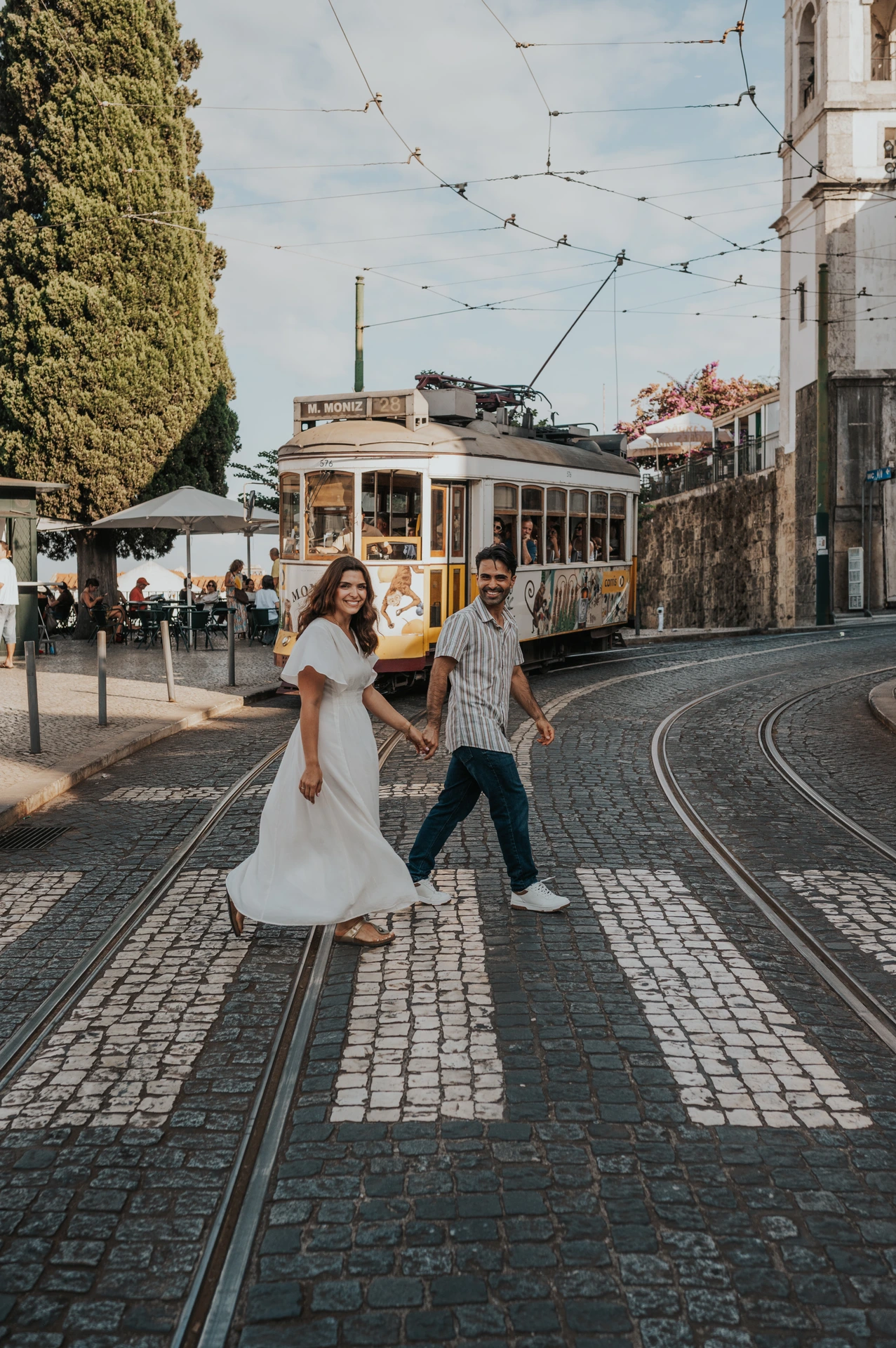 Couple main dans la main dans une rue pavée avec un tramway jaune de Lisbonne à l’arrière-plan