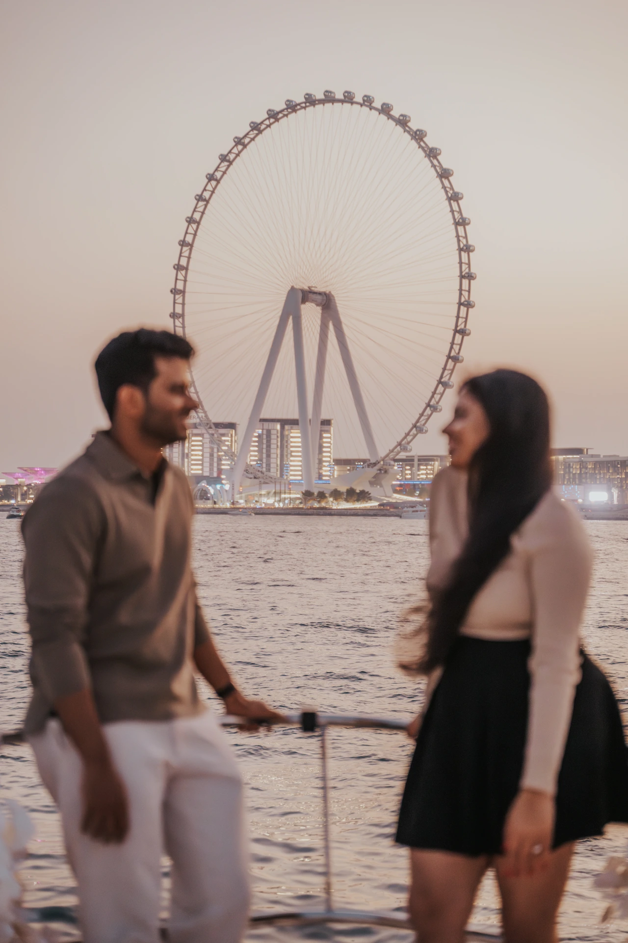 Dubai Couple Photoshoot - boat with Ain view A couple is photographed on a boat during a Dubai couple photoshoot, with Ain Dubai visible behind them for a destination-style waterfront frame.