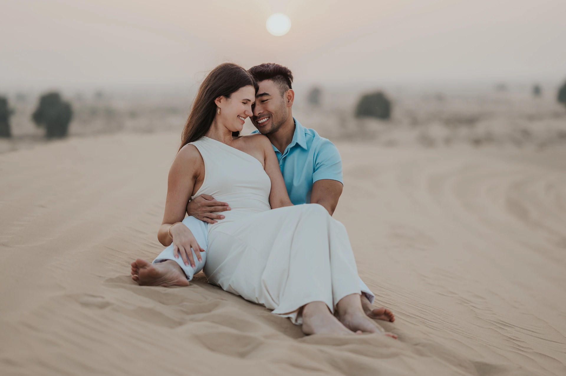 Dubai Couple Photoshoot - sunset dunes portrait A couple stands close in Dubai dunes during a couple photoshoot, using sunset tones and open desert space for intimate and cinematic framing.