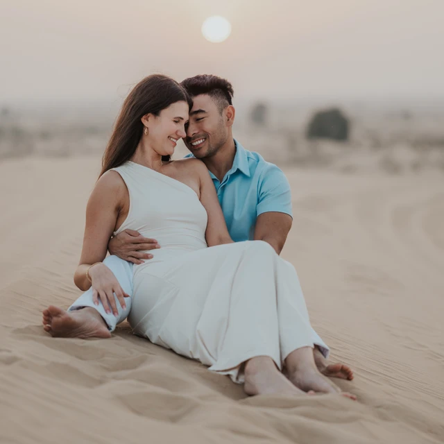 Dubai Couple Photoshoot - sunset dunes portrait A couple stands close in Dubai dunes during a couple photoshoot, using sunset tones and open desert space for intimate and cinematic framing.