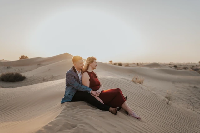 A couple sits together on Dubai sand dunes in warm golden light during a sunset photoshoot.