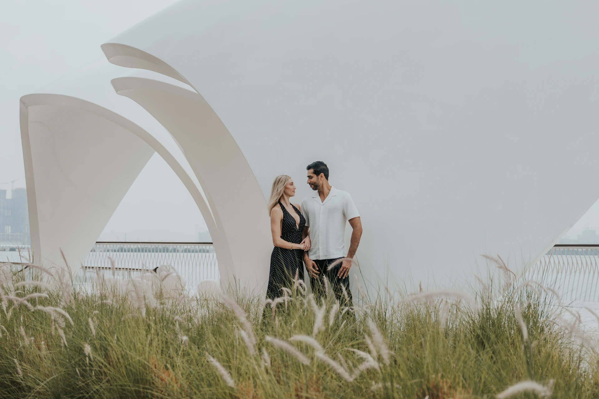 A couple stands beneath a modern architectural structure with skyline views in Dubai.
