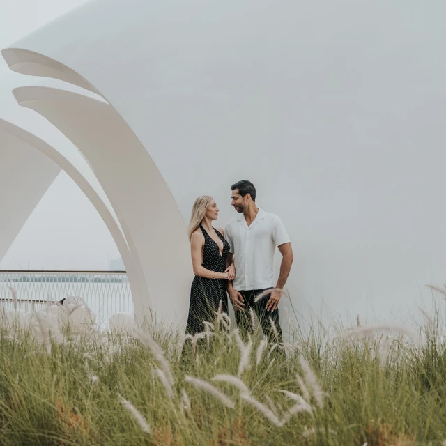 A couple stands beneath a modern architectural structure with skyline views in Dubai.