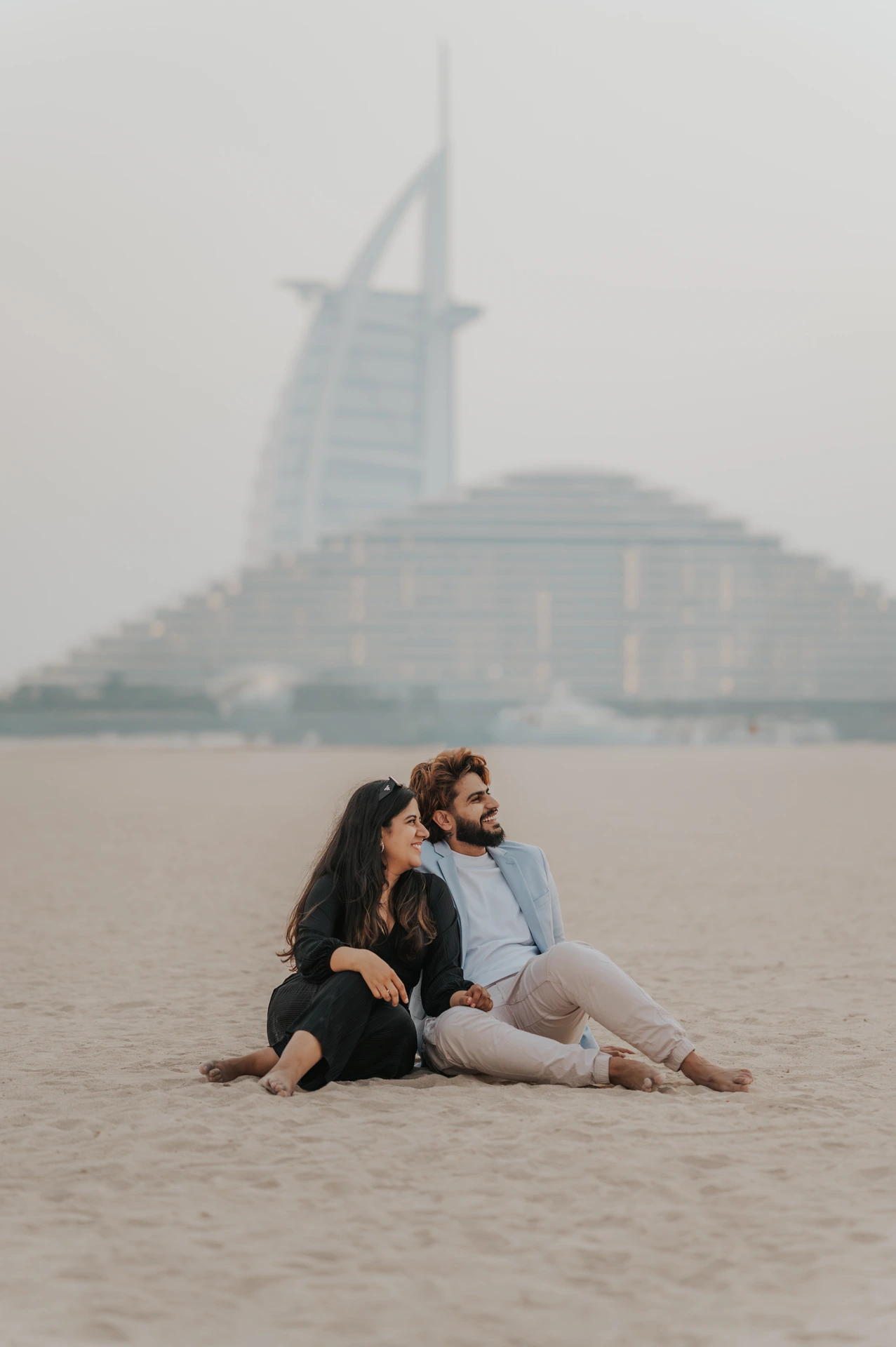 A couple embraces on a Dubai beach with Burj Al Arab softly visible in the background.