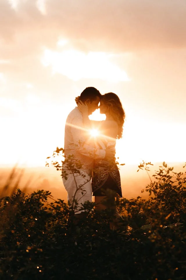 Couple with sun behind them going down kissing, sun in between their bodies