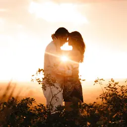 Couple with sun behind them going down kissing, sun in between their bodies