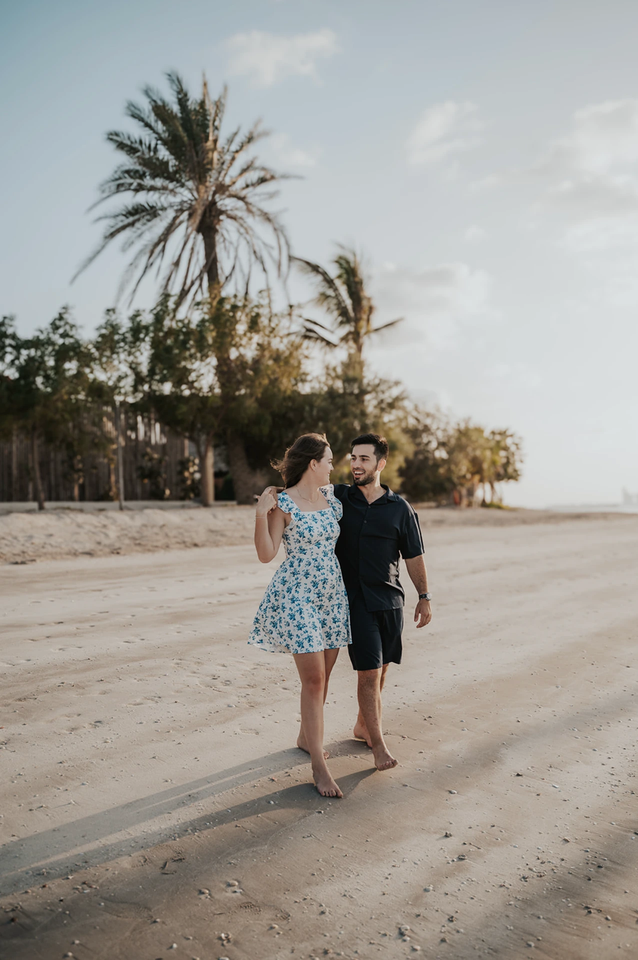 A couple smiles and plays on the beach in Dubai while walking through warm sunrise light.