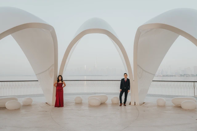 A couple stands apart under the white architectural arches at Dubai Creek Harbour during a couple photoshoot, with soft waterfront haze in the background. A couple stands apart under the white architectural arches at Dubai Creek Harbour during a couple photoshoot, with soft waterfront haze in the background.