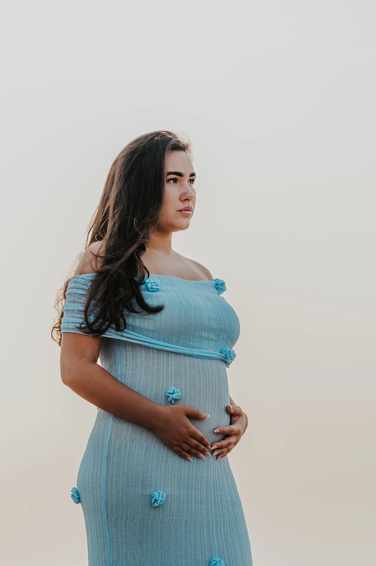 Pregnant woman in a light blue dress poses in profile, hands on belly, during a Dubai maternity photoshoot.