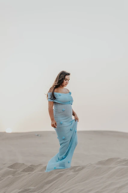 Babymoon photoshoot Dubai location Pregnant woman in a light blue dress stands on Dubai desert dunes during a serene maternity photoshoot.