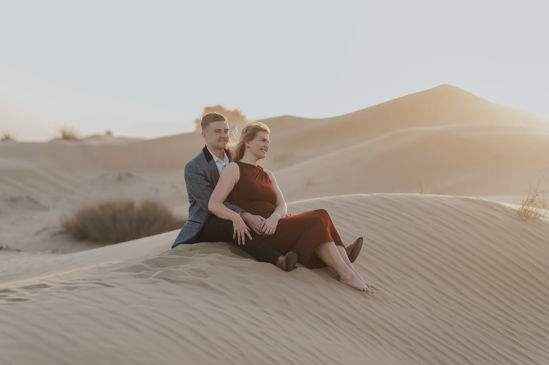A couple sits on a dune ridge in Dubai with warm evening light, captured in a romantic desert couple photoshoot.