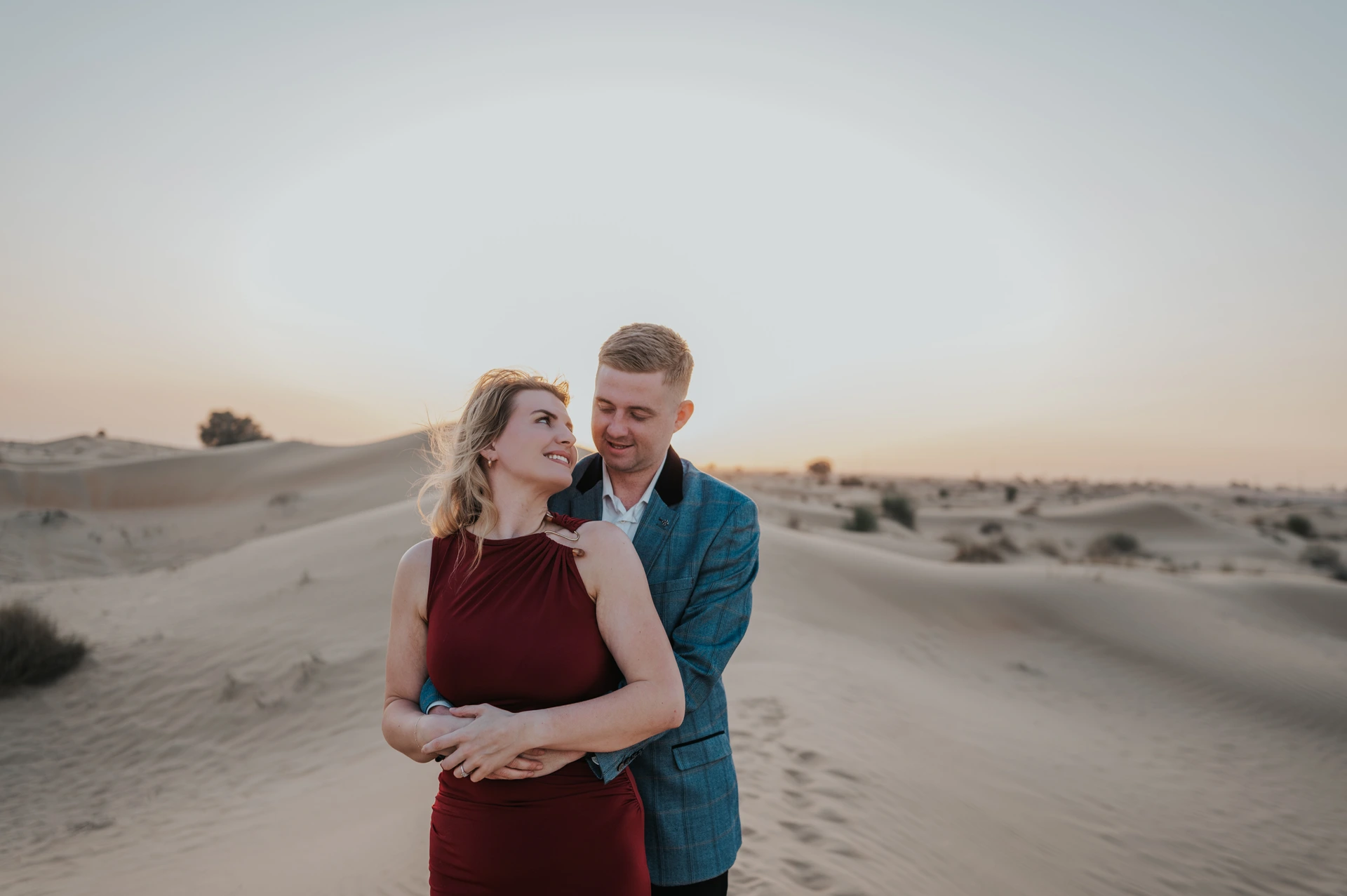 A couple in formal outfits embraces on Dubai dunes at golden hour during a desert couple photoshoot.