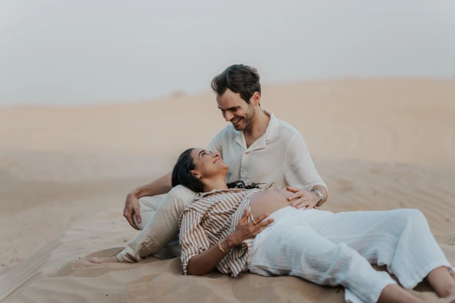Maternity Photoshoot Desert Dubai - planning support An expecting couple sits together on Dubai desert dunes during a maternity photoshoot, sharing a relaxed and affectionate hero-style pose.