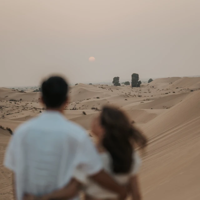 Dubai Desert proposal Couple blurry in the foreground with the sun sharp in the background during their proposal in the Dubai desert