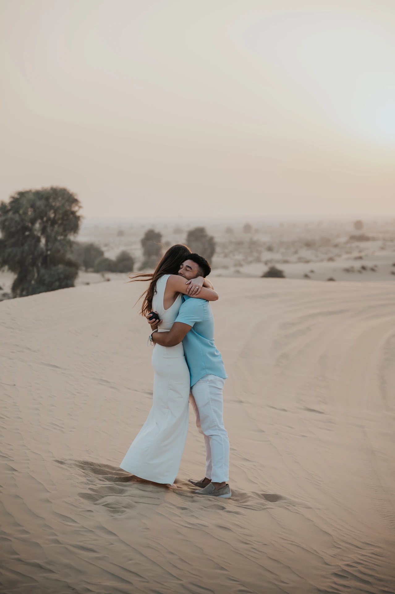 A couple poses beside a red off-road vehicle on Dubai dunes during a desert proposal photoshoot.
