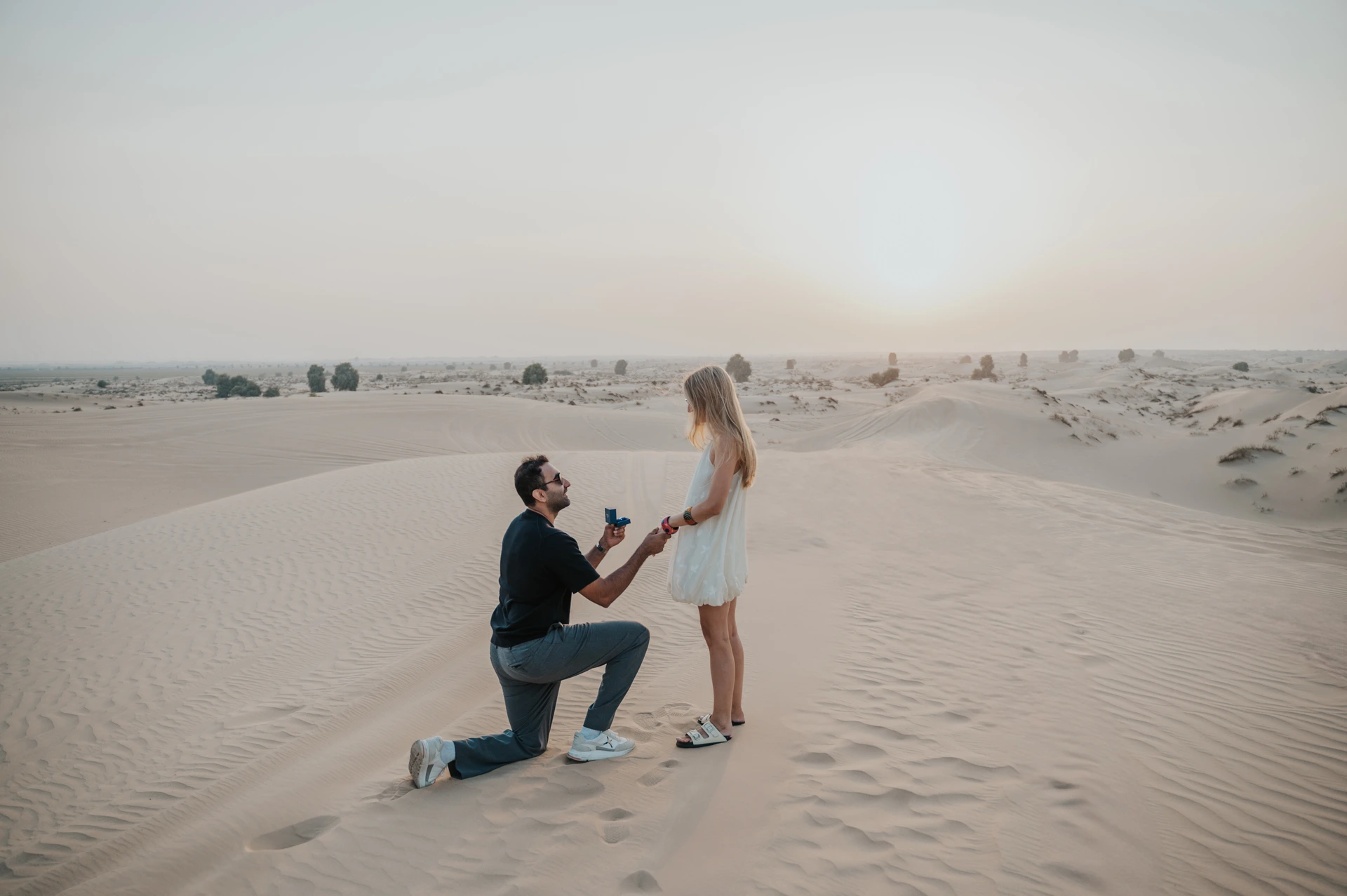 A couple strolls hand in hand on Dubai dunes at sunset after a proposal moment.