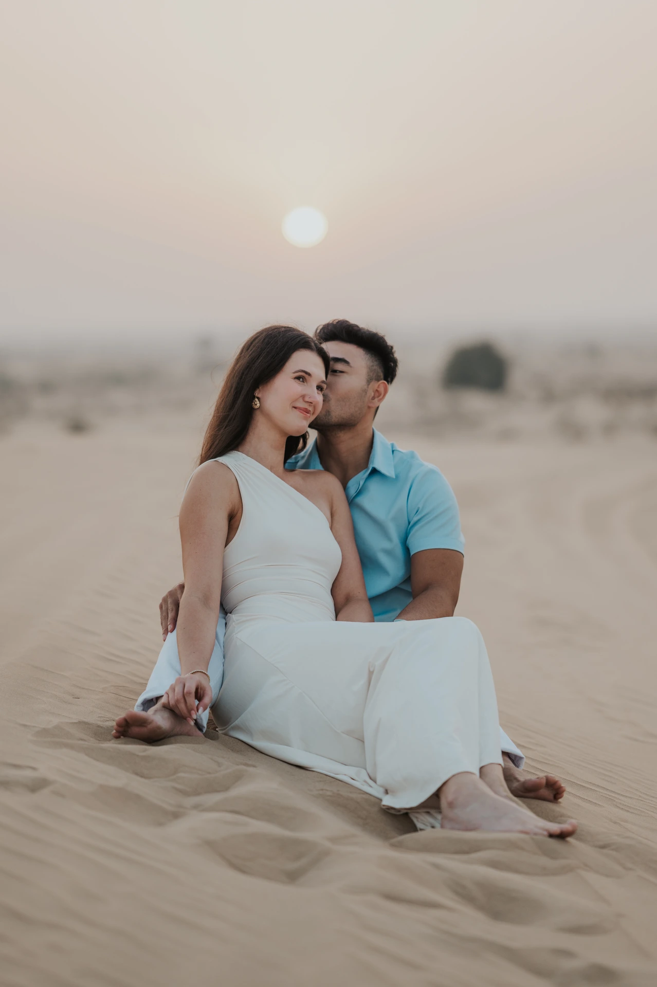 A couple sits close together on a dune in Dubai at sunset during a desert proposal session.