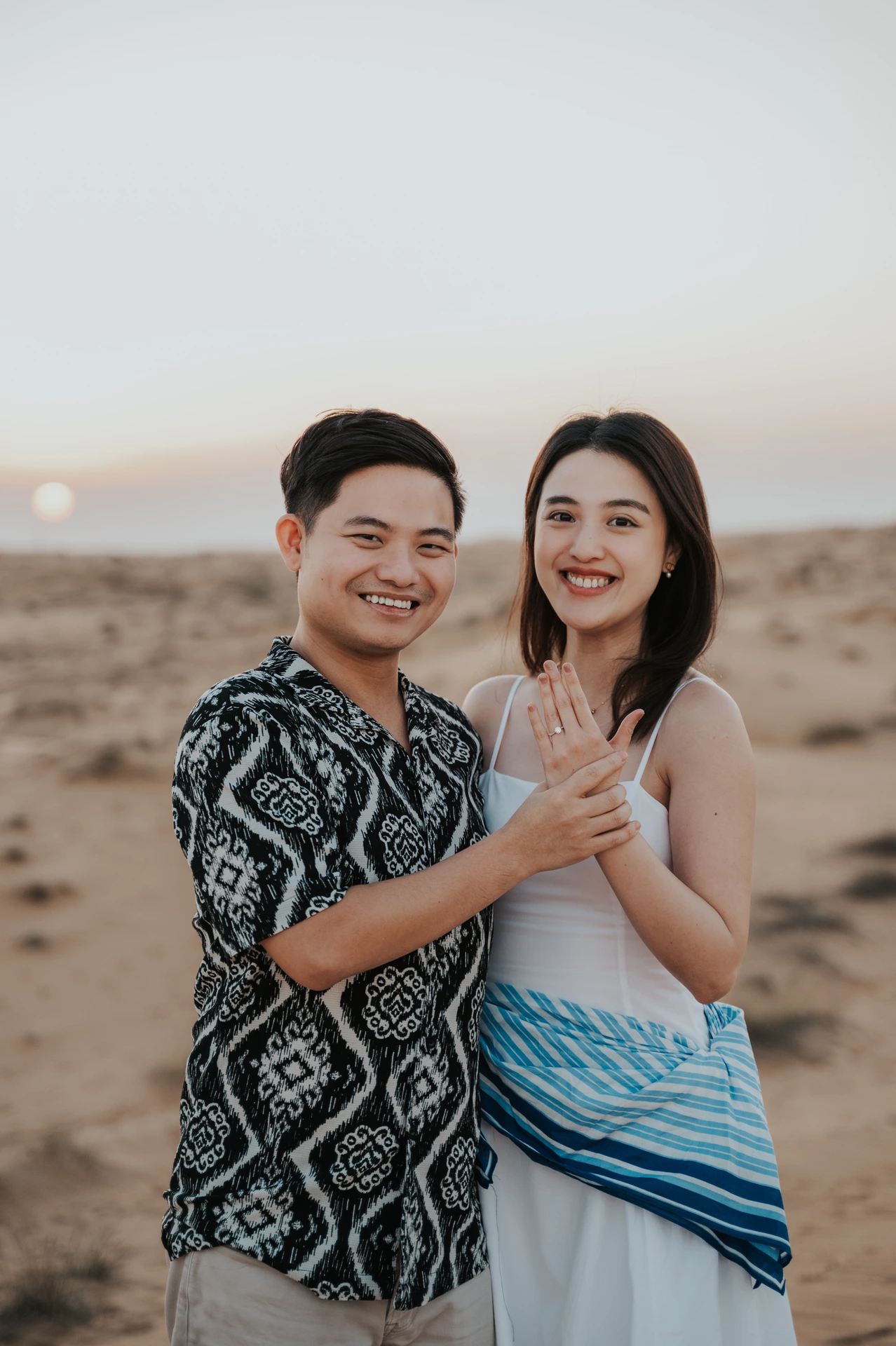 A smiling couple in the Dubai desert shows the engagement ring after the proposal.
