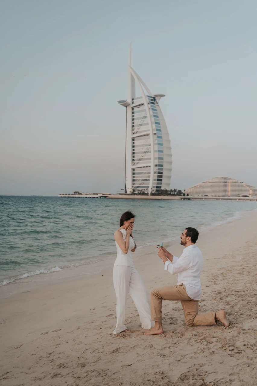 Beach proposal Dubai - Sunset proposal with Burj Al Arab view A man proposes on the shoreline at sunset while his partner reacts, with Burj Al Arab visible behind them.