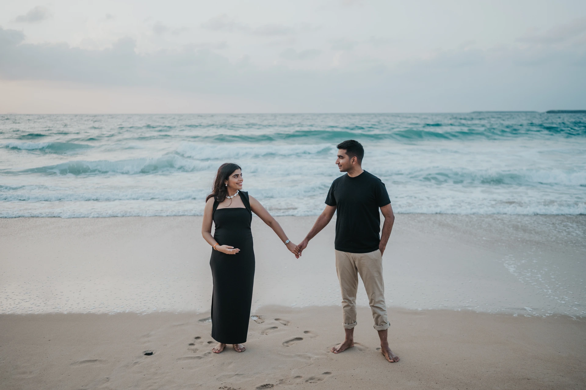 A close beach portrait of an expecting couple holding hands and smiling during a relaxed Dubai babymoon photoshoot.