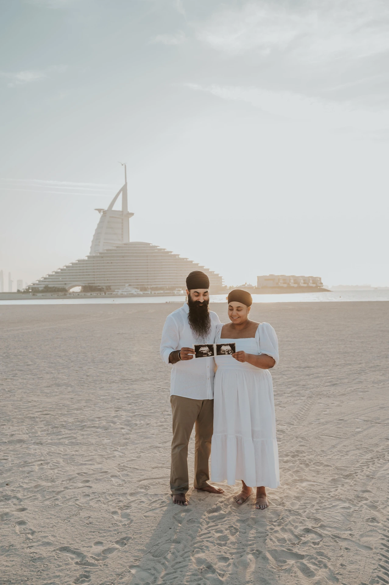 A maternity couple portrait on the Dubai shoreline with iconic Burj Al Arab views behind them.