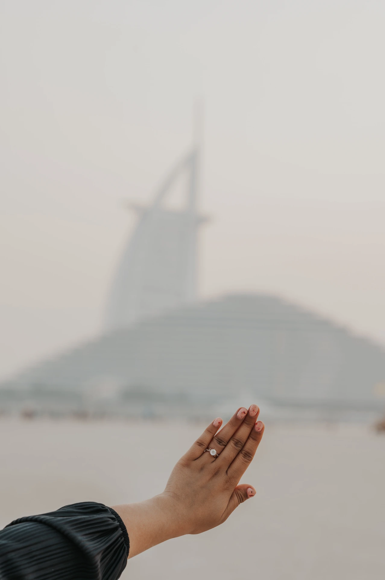 Close-up of an engagement ring being placed on a hand, with Burj Al Arab softly blurred in the background.