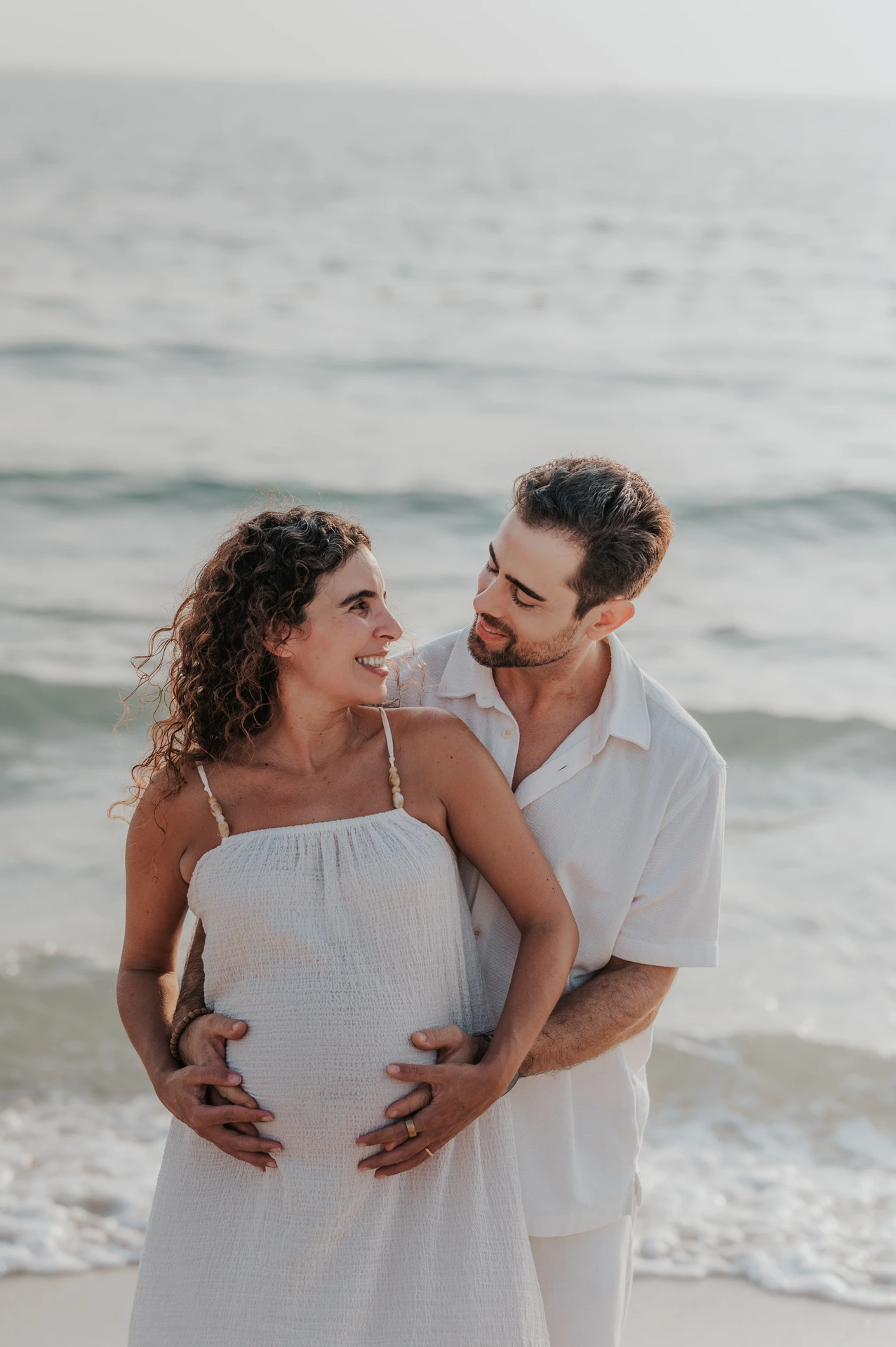 A close-up of an expecting couple smiling together by the sea during a Dubai maternity session.