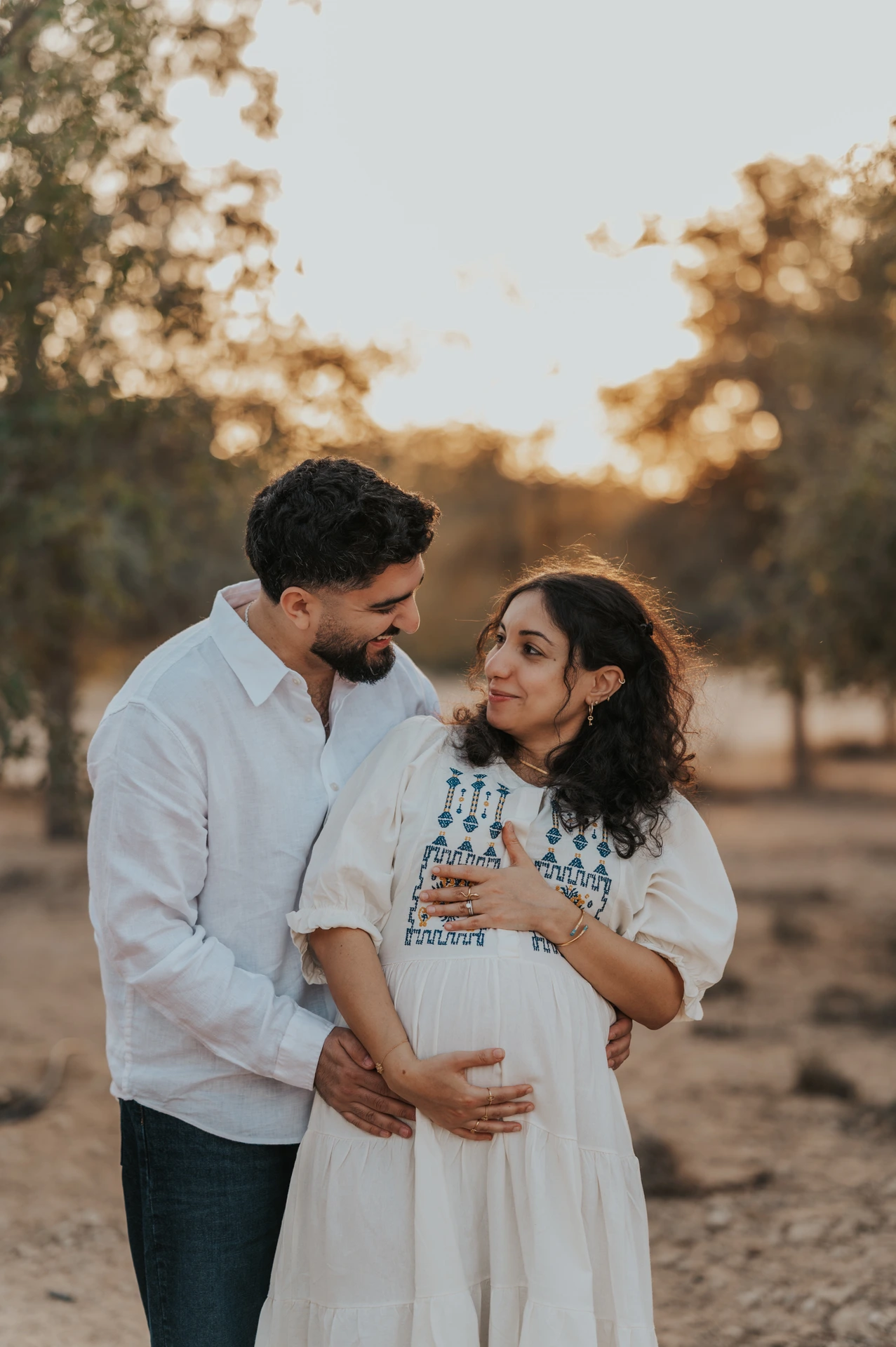 A couple shares an intimate maternity portrait in a natural setting with soft golden tones.