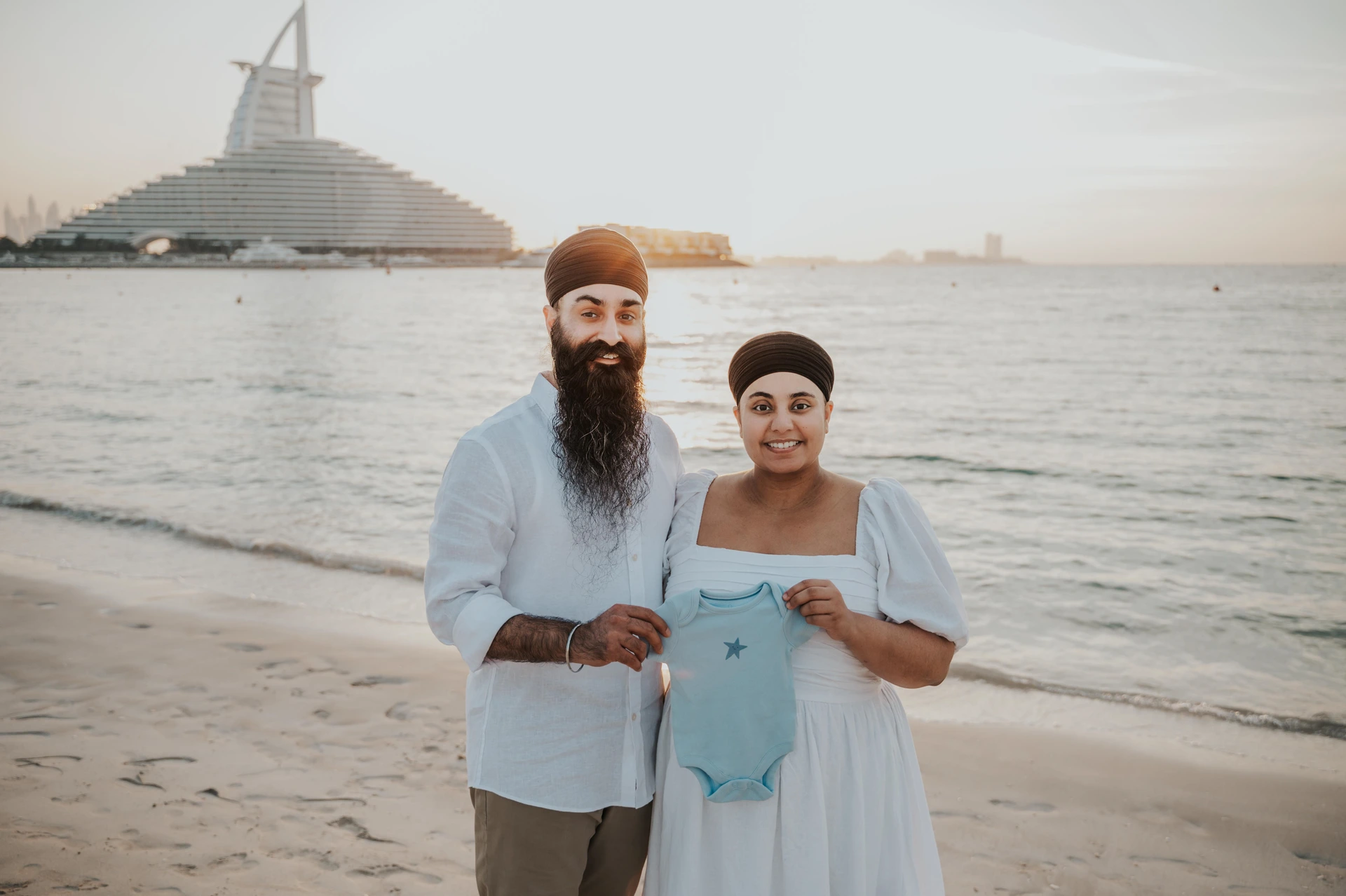 An expecting couple stands calmly on Dubai beach with Burj Al Arab behind them during a maternity photoshoot planning example.