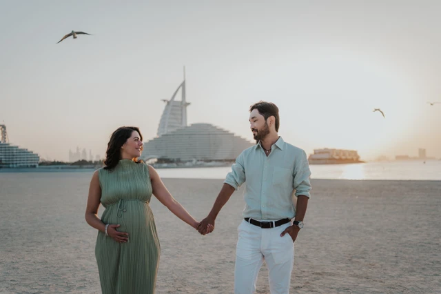 A close portrait captures an expecting couple embracing on Dubai beach with Burj Al Arab softly visible during a maternity photoshoot.