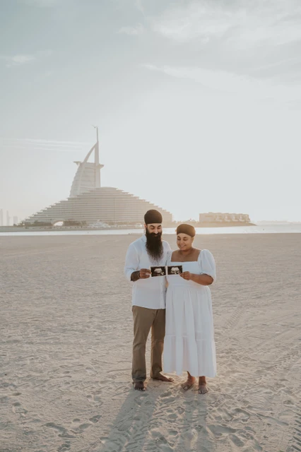 Burj Al Arab maternity photoshoot Dubai - timing guide example An expecting couple stands on Dubai beach with Burj Al Arab behind them during a maternity photoshoot used for timing guidance.