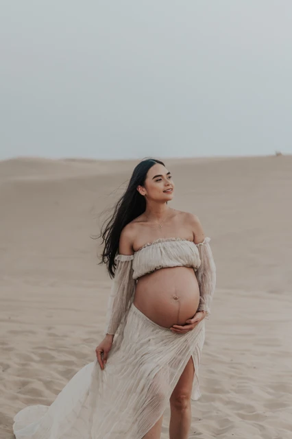 A pregnant woman poses in a flowing dress on Dubai dunes during a maternity desert photoshoot.