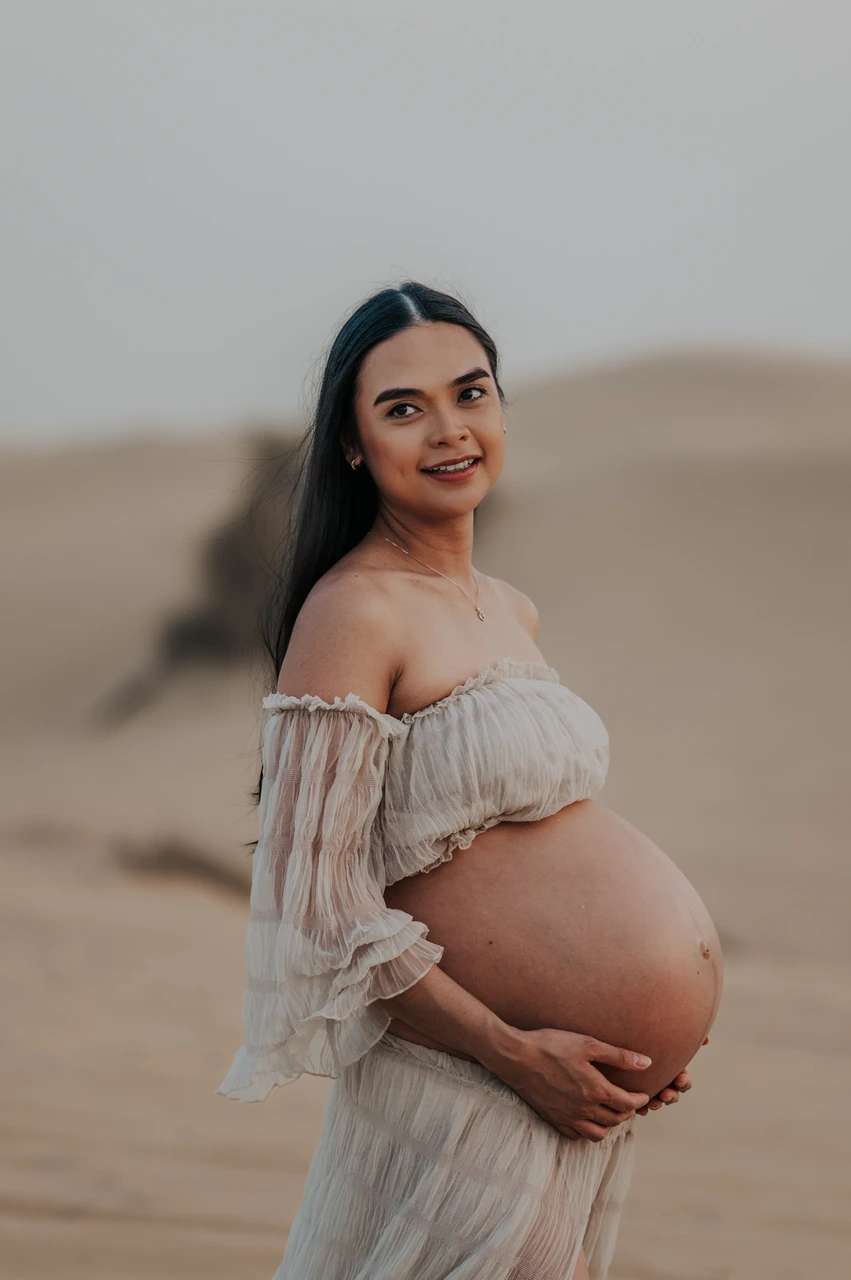 Dubai maternity desert photoshoot guide - close bump portrait An expecting mother poses on Dubai dunes during a maternity desert photoshoot at sunset.