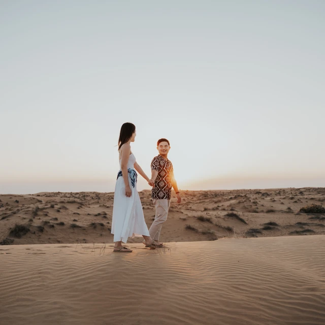 Dubai Engagement Photoshoot - dunes movement frame A couple walks through Dubai dunes in an engagement photoshoot, with natural movement and neutral styling suited to open desert compositions.