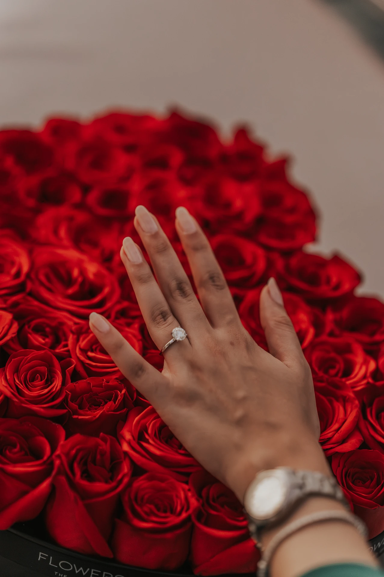 Ein Foto, aufgenommen von einem Heiratsantrag-Fotografen in Dubai, das die Hände der Frau vor wunderschönen roten Rosen zeigt, mit dem Fokus auf dem Diamantring.