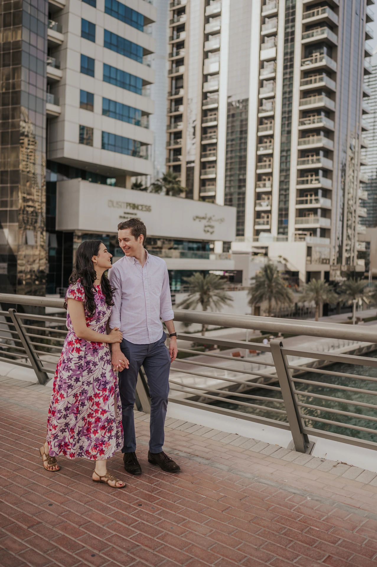 A couple holding hands on Dubai Marina promenade among high-rises during a relaxed proposal photoshoot.