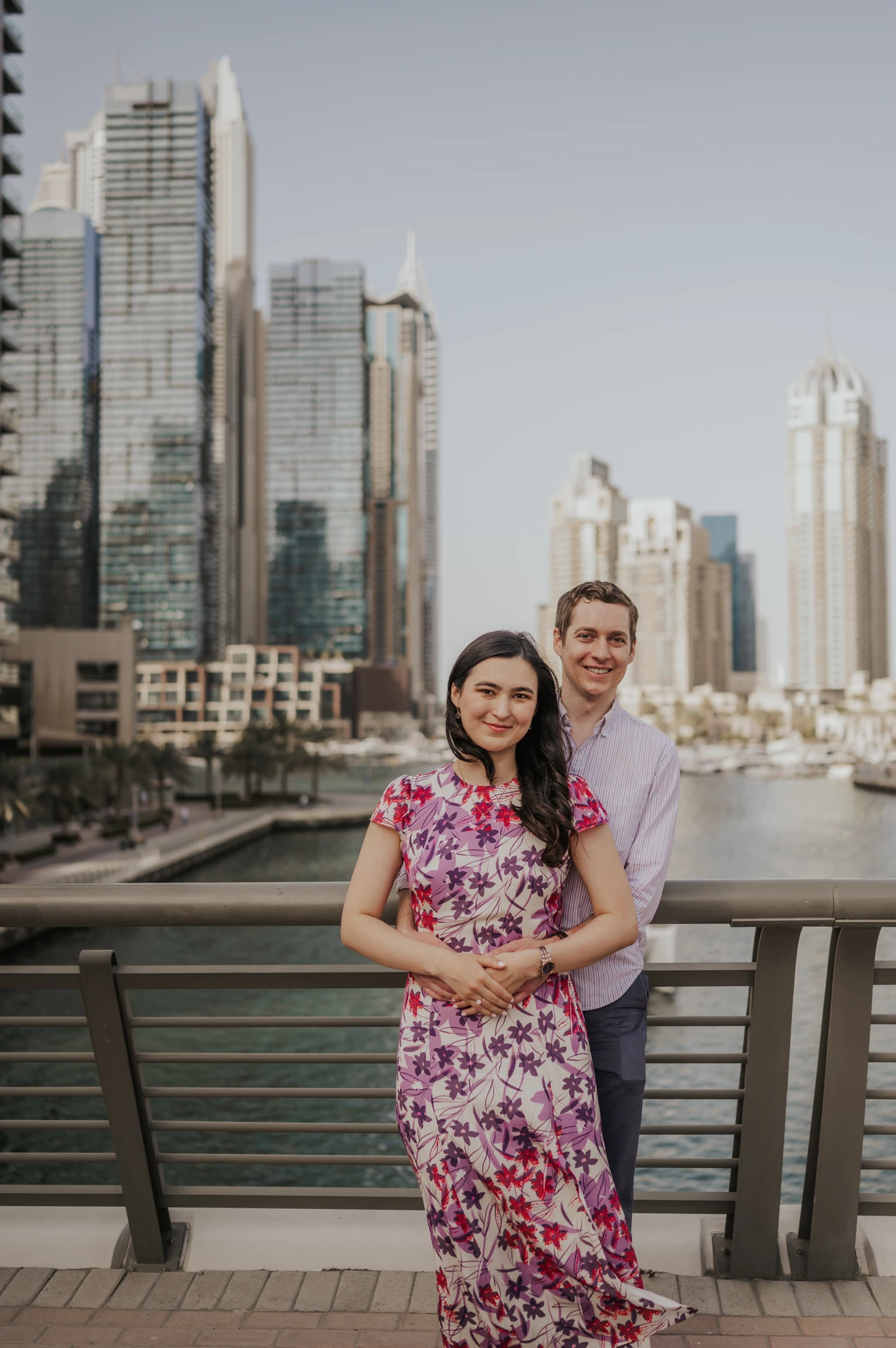 A couple embraces on a waterfront bridge in Dubai Marina at sunset during a romantic proposal session.