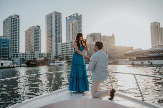 Dubai Marina proposal at sunset A man proposes on a yacht in Dubai Marina at sunset while his partner smiles and holds his hand.
