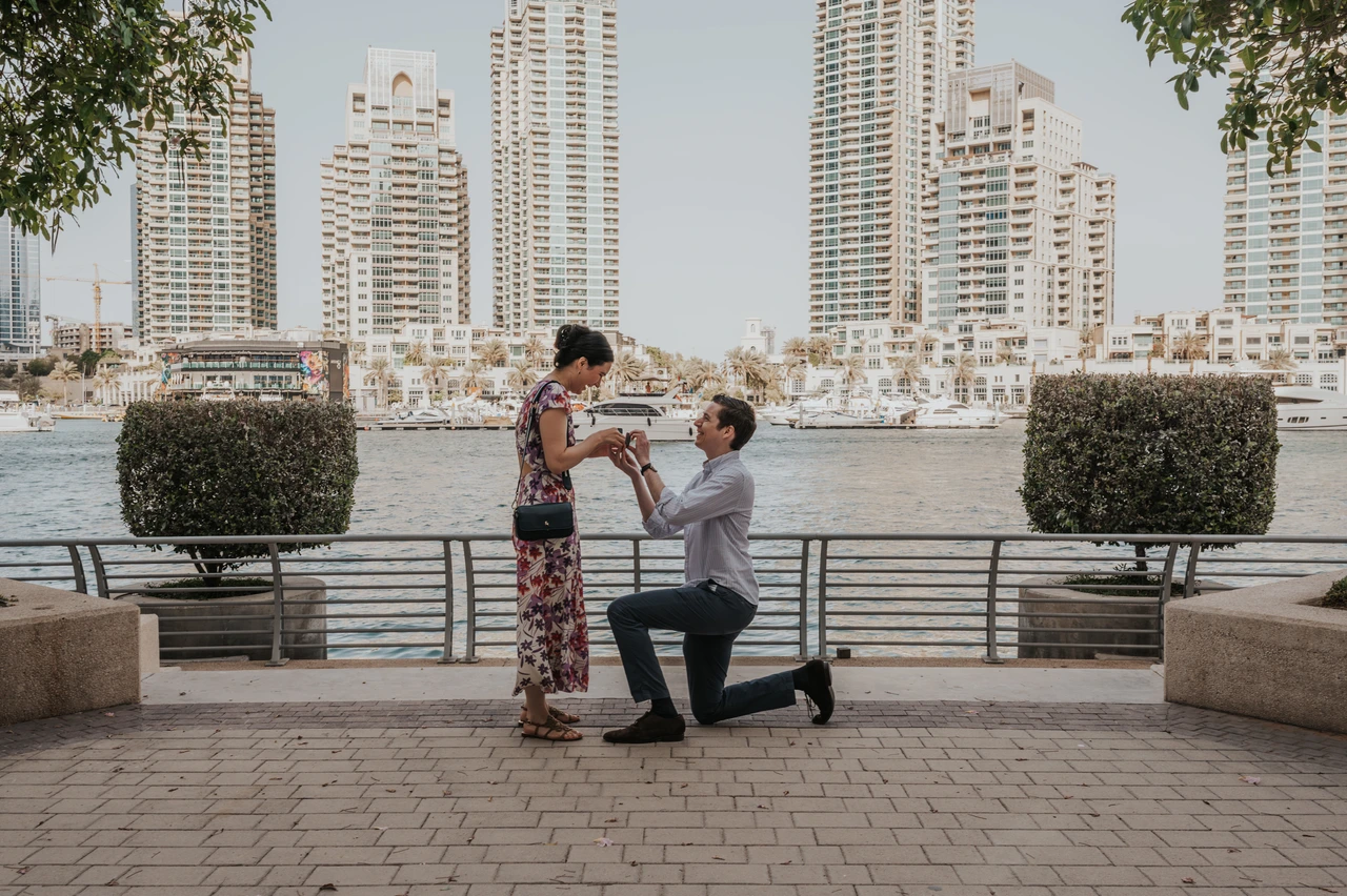 Dubai Marina proposal on Marina Walk A man kneels to propose on Dubai Marina Walk with waterfront views and high-rise towers in the background.