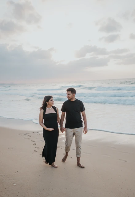 An expecting couple stands by the shoreline in Dubai during a maternity photoshoot, highlighting the relaxed outdoor beach style with soft evening light.