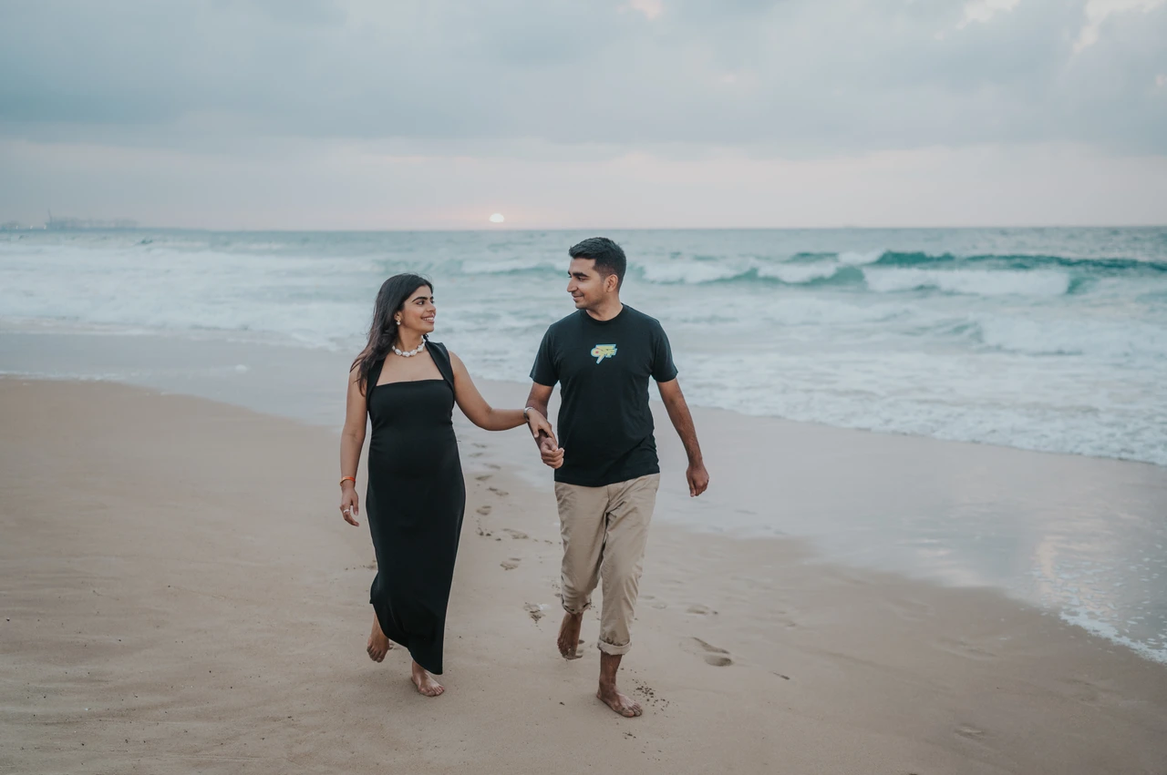 Maternity photoshoot beach vs desert - seaside walking couple An expecting couple walks along the Dubai shoreline during a maternity photoshoot, showing movement and connection in an outdoor beach session.